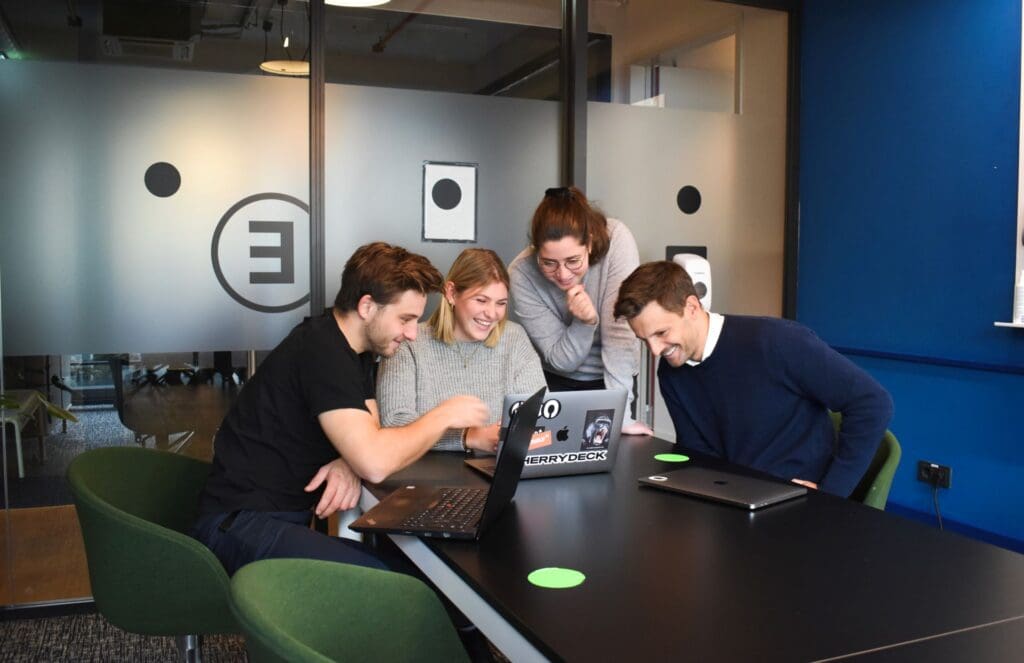 an image of four people gathered around a laptop to discuss approaches to OKR Scoring